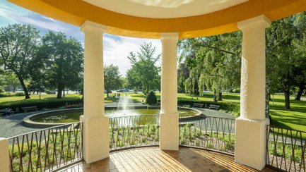 Blick aus dem Pavillon auf den sonnigen Peiner Stadtpark mit Wegen, Bäumen und Geländer.