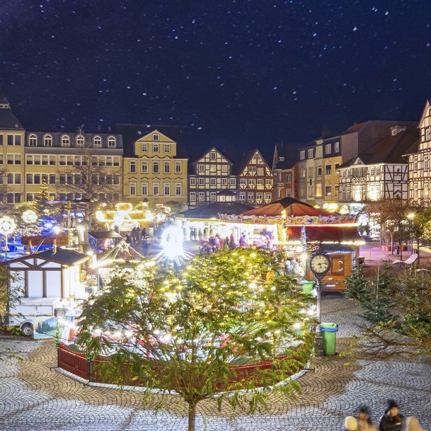 Weihnachtlich beleuchteter Marktplatz mit geschmücktem Baum, historischen Fachwerkhäusern und mehreren Marktständen bei Nacht.