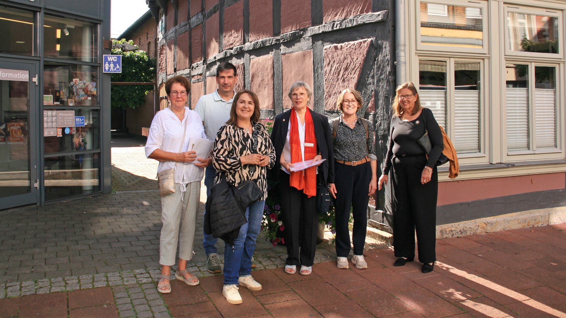 Eine Gruppe von Menschen steht vor einem Fachwerkhaus und einem Anbau mit der Aufschrift Tourist-Information.