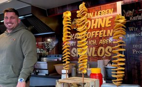 Streetfood-Stand auf dem Food Truck Festival in Peine mit frisch frittierten Spiralkartoffeln am Spieß und lächelndem Standbetreiber im Hintergrund.