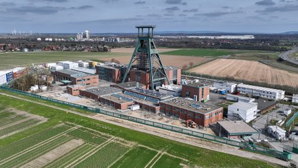 Das Bild zeigt aus der Vogelperspektive Gebäude mit einem Förderturm sowie die umliegende Landschaft.  