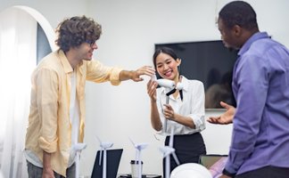Drei Personen diskutieren um einen Tisch mit Miniatur-Windrädern, Bauhelmen und Laptops in einem Büro.