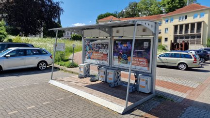 BikePort Peine mit überdachter eBike-Ladestation und Informationsflächen auf einem Parkplatz vor einem Gebäude.