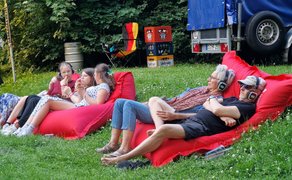 Silent Disco in Peine: Mehrere Generationen entspannen gemeinsam auf roten Sitzsäcken im Grünen, tragen Funkkopfhörer und genießen die Musik in ruhiger Open-Air-Atmosphäre.