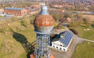 Luftaufnahme eines alten Kugelwasserturms auf einem Industriegelände mit angrenzendem Gebäude und weiteren Industrieanlagen im Hintergrund