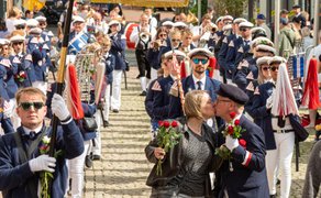 Schützenumzug beim Peiner Freischießen mit Musikkapelle in Uniform, Fahnen und einem Paar, das sich am Straßenrand mit Rosen küsst.