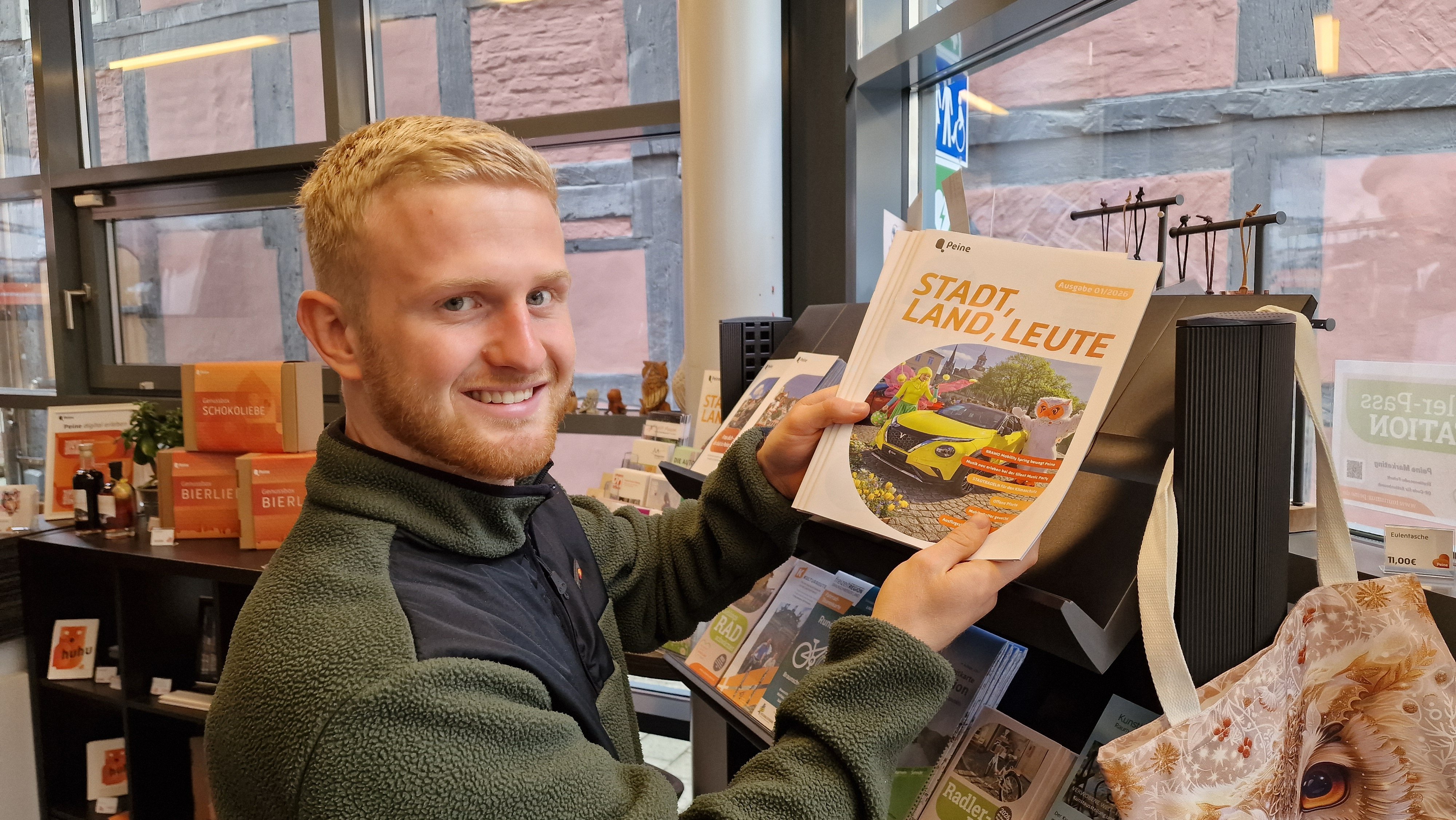 Person hält mehrere Ausgaben der Zeitschrift »Stadt, Land, Leute« mit Titelbild eines gelben Autos und Personen in Kostümen.