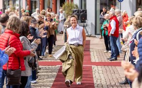 Eine Frau läuft über einen roten Teppich durch eine Gasse aus applaudierenden Menschen in der Peiner Innenstadt, während Zuschauer links und rechts stehen und die Szene einer Modenschau unter freiem Himmel verfolgen.