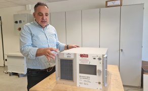 Ein Mann deutet auf ein technisches Gerät, das auf einem Tisch steht.