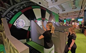 Das Bild zeigt eine Frau beim Wurf auf eine Dartscheibe.