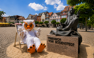 Uhlinchen sitzt in einem Liegestuhl neben dem Denkmal von Friedrich von Bodenstedt auf dem Marktplatz in Peine.
