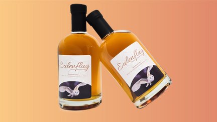 Zwei Flaschen Haselnusslikör „Eulenflug“ aus Peine vor farbigem Hintergrund, regionale Spezialität mit Eulenmotiv auf dem Etikett.