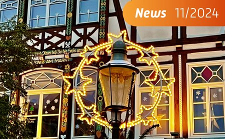 DAs Bild zeigt eine Weihnachtsbeleuchtung in Nahaufnahme, im Hintergrund befindet sich ein weihnachtlich geschmücktes Fachwerkhaus. 