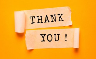 Zwei Papierstreifen auf gelbem Hintergrund mit der aufgedruckten Aufschrift „THANK YOU!“, dekorativ angerollt und mittig angeordnet.
