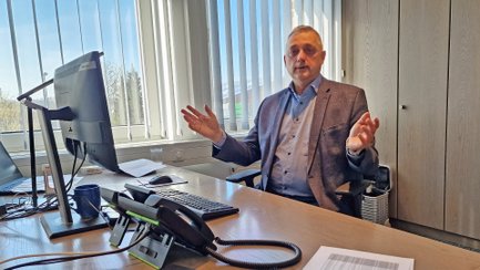 Hanke-Geschäftsführer Olaf Küpper sitzt an seinem Schreibtisch mit Computer und Telefon vor einem Fenster und gestikuliert mit beiden Händen.