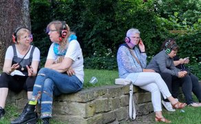 Besucher der Silent Disco im Schlosspark Peine sitzen entspannt auf einer Steinmauer und hören mit Funkkopfhörern Musik – ruhige Momente abseits der Tanzfläche.