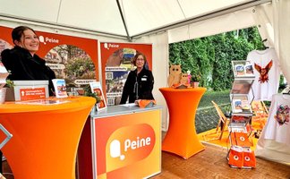 Messestand von Peine Marketing beim Entdeckertag mit orangefarbenen Infoständen, Informationsmaterialien und zwei Mitarbeiterinnen.