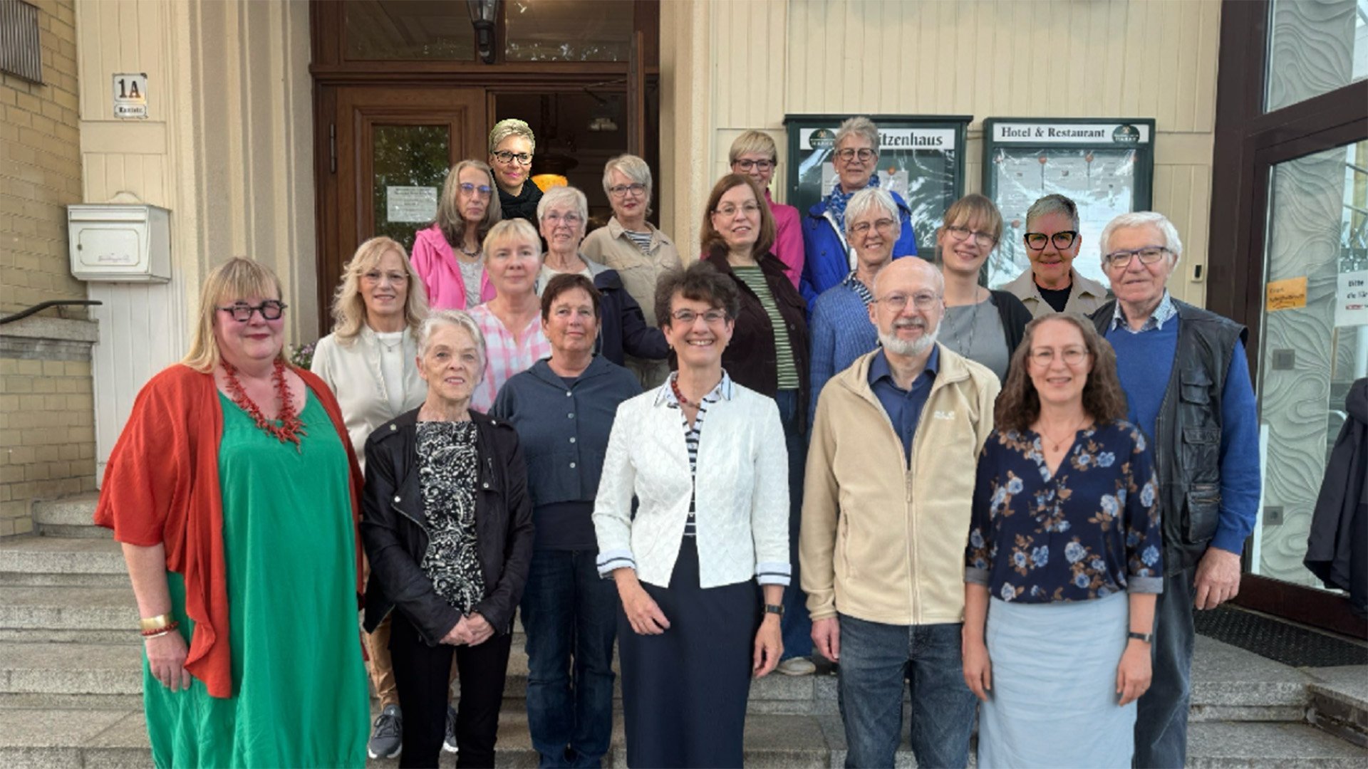 Gruppenfoto von rund 20 Personen unterschiedlichen Alters, die vor einem Gebäude gemeinsam für die Kamera posieren.