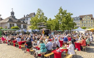Zahlreiche Besucher sitzen an langen Tischen auf dem Marktplatz in Peine und genießen eine öffentliche Veranstaltung bei sonnigem Wetter