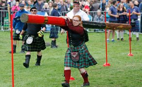 Teilnehmerin im Kilt trägt Baumstamm beim Highland Game „Tree Trunk Slalom“ durch Parcours vor Publikum im Peiner Stadtpark