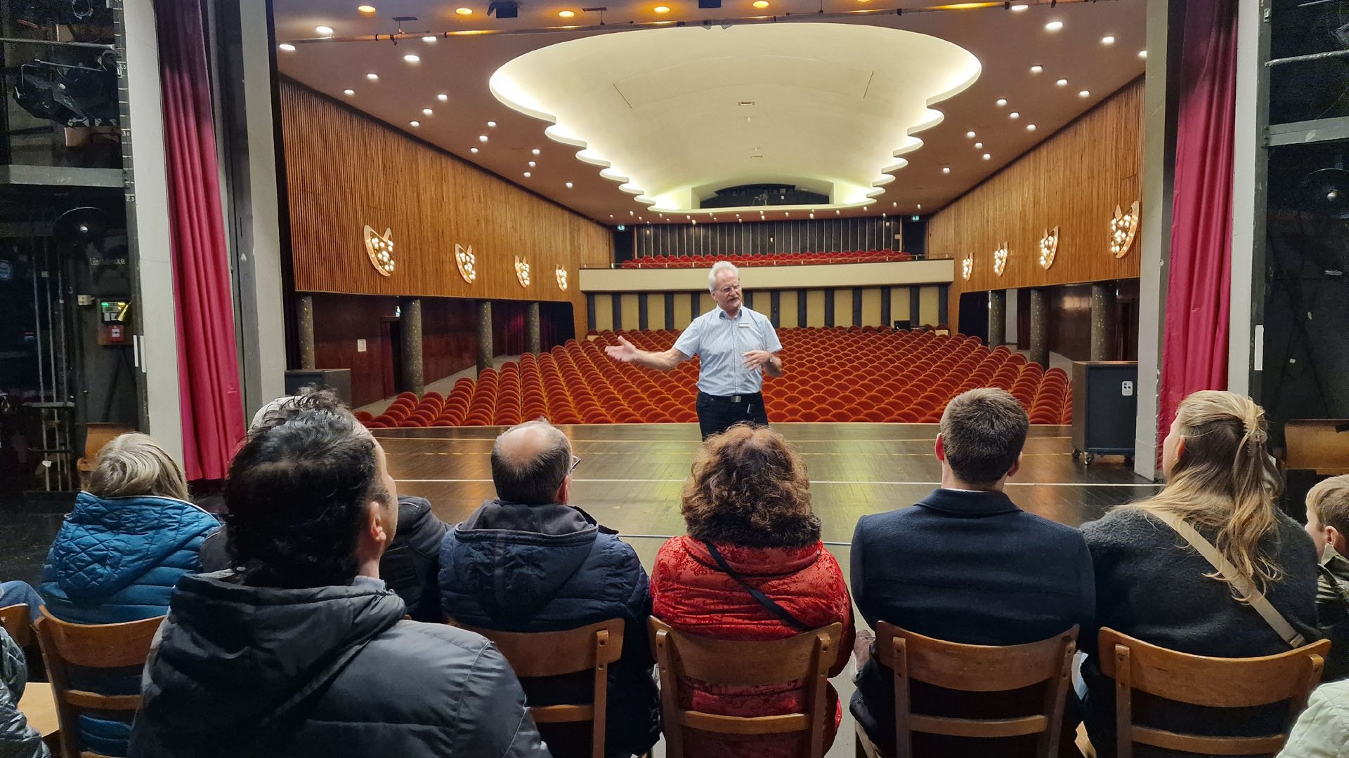 Das Bild zeigt eine Gruppe von Menschen sitzend auf der Bühne des Stadttheaters mit Blick auf den Zuschauersaal.