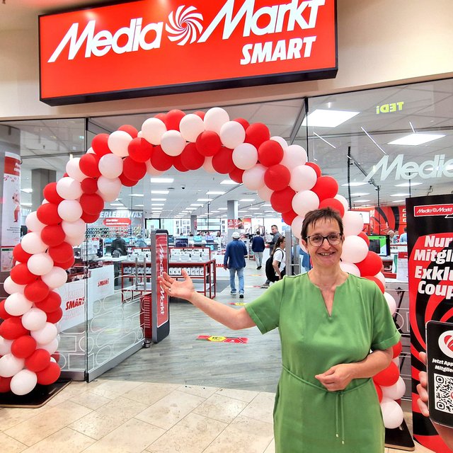 Eingangsbereich des neuen MediaMarkt SMART in der City Galerie Peine mit rotem Ballonbogen zur Eröffnung. Vor dem Markt begrüßt ein Mitarbeiter die Besucher des kompakten Elektronikfachmarkts.