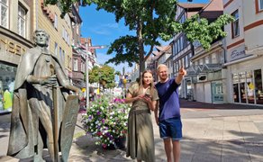 Zwei Teilnehmende stehen neben einer Statue in der Innenstadt von Peine und orientieren sich per Smartphone während einer digitalen Stadtrallye.