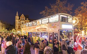 Doppeldeckerbus mit Aufschrift 'ESSEN WISSEN' auf einem belebten Weihnachtsmarkt mit festlicher Beleuchtung und Menschen in Winterkleidung.