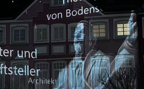 Detailaufnahme einer Videomapping-Projektion mit historischen Persönlichkeiten und Schriftzügen auf einer Gebäudefassade in der Peiner Innenstadt bei Nacht.