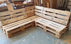 Ecksofa aus hellen Holzpaletten mit Rückenlehne in einer Werkstatt.