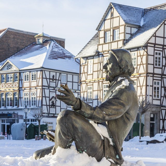 Statue auf dem verschneiten Marktplatz in Peine mit historischer Fachwerkarchitektur im Hintergrund bei winterlichem Sonnenschein.