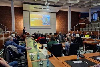 Menschen sitzen in einem Konferenzraum bei einer Veranstaltung zum Immobiliendialog, während vorne eine Präsentation gezeigt wird – Austausch zu Leerständen, Immobilien und Innenstadtentwicklung.