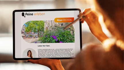 Eine Person hält ein Tablet in der Hand. Auf dem Display ist der digitale Newsletter „Peine erleben“ geöffnet, der mit Bildern und Beiträgen zu Veranstaltungen, Freizeitangeboten und Erlebnissen in Peine gefüllt ist. Im Hintergrund ist eine unscharfe grüne Parklandschaft zu sehen.