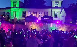 Das Bild zeigt tanzende Menschen im Burgpark in Peine im Discolicht bei der Silent Music Party in Peine. 