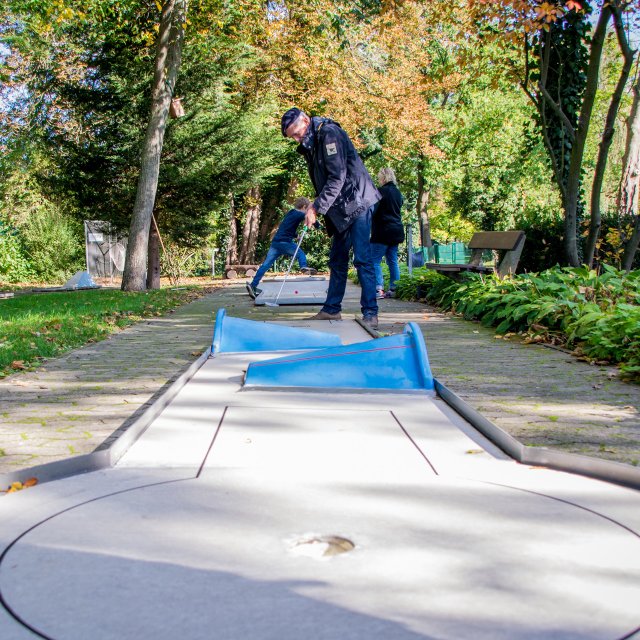 Das Bild zeigt einen Mann, der einen Minigolfschläger in der Hand hält und zum Schlag ansetzt. 