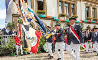 Fahnenträger in historischen Uniformen ziehen während des Peiner Freischießens über den Marktplatz.