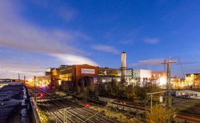Industrieanlage mit Schornstein und Gleisen und dem Schriftzug 'Peiner Träger' im Vordergrund bei Abenddämmerung unter blauem Himmel. 