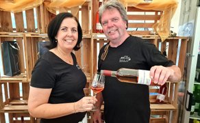 Zwei Personen schenken beim Peiner Weinfest Roséwein in ein Weinglas vor einem Weinstand ein.