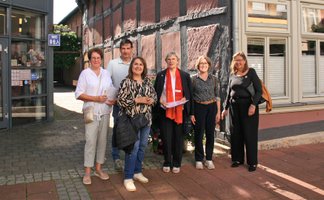 Eine Gruppe von Menschen steht vor einem Fachwerkhaus und einem Anbau mit der Aufschrift Tourist-Information.