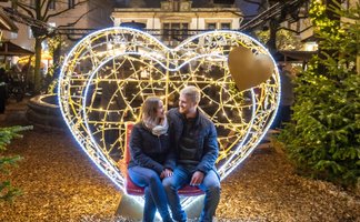 Das Bild zeigt ein Pärchen, das sich anschaut und dabei im beleuchteten Herz sitzt. Einer XXL-Lichtfigur in der Weihnachtsstadt Peine.