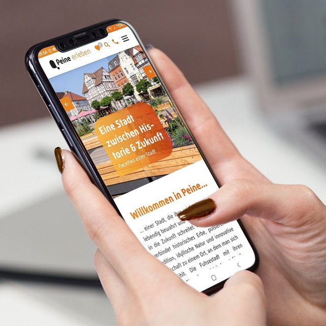 Eine Person hält ein Smartphone in der Hand und ruft die mobile Website „Peine erleben“ mit Informationen über die Stadt Peine auf.