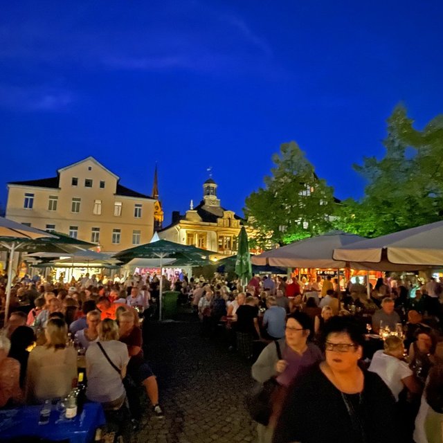 Peiner Weinfest am Abend mit dicht gedrängten Besucherinnen und Besuchern unter Sonnenschirmen, beleuchtetem Marktplatz, historischen Gebäuden im Hintergrund und stimmungsvoller Atmosphäre in der Innenstadt von Peine.