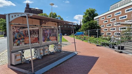 BikePort Peine mit überdachter eBike-Ladestation und Informationsflächen auf einem Parkplatz vor einem Gebäude.