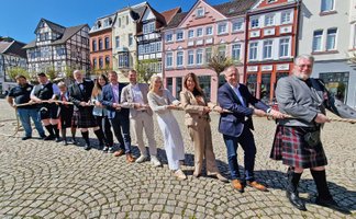 Gruppe von Teilnehmenden zieht Tau vor historischer Fachwerkkulisse auf dem Marktplatz in Peine