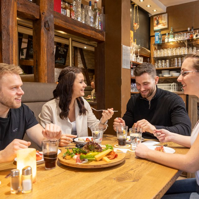 Das Bild zeigt eine Gruppe junger Menschen, die in einem Restaurant sitzen und Speisen und Getränke genießen. 