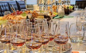 Mit Whisky gefüllte kleine Gläser stehen auf einem eingedeckten Tisch im Vordergrund. 