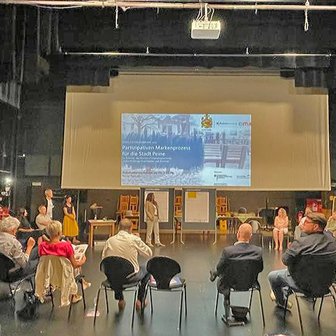 Das Bild zeigt Menschen, die auf der Bühne im Stadttheater Peiner Festsäle sitzen und an einem Workshop teilnehmen. 