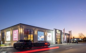 Das Rausch Schokoladenhaus Peine zeigt sich in der Abenddämmerung als modern beleuchtete Chocolaterie in Peine, mit großformatigen Schokoladenmotiven an der Fassade. Die Außenaufnahme unterstreicht Genuss, Café und Schokolade in Peine als hochwertiges Ziel für Kulinarik und Süßwaren.