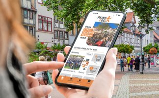 Das Bild zeigt eine Frau, die ein Handy in der Hand hält, auf dem die City App Peine2Go zu sehen ist.