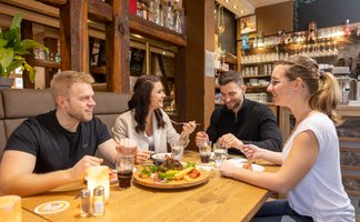 Das Bild zeigt eine Gruppe junger Menschen, die in einem Restaurant sitzen und Speisen und Getränke genießen. 